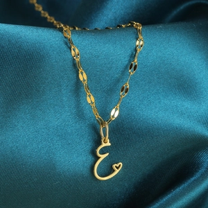 Macro-opname van de gouden olijfketting en hartvormige letter E-hanger op zijde