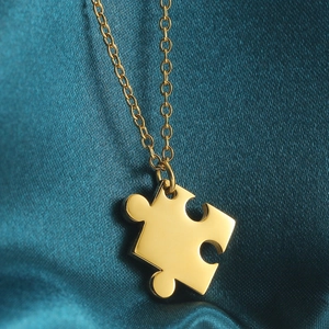 Close-up of a polished gold puzzle piece pendant on a dark silk fabric background