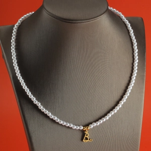 Detail of pearl necklace with gold letter B pendant on a display stand with red background