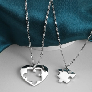Detail of silver heart puzzle pendant necklaces with polished finish on blue silk background