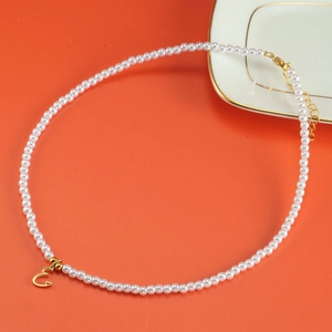 Detail of pearl necklace with gold letter E pendant and lobster clasp on orange backdrop