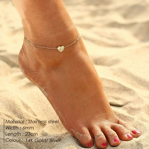 Detail of 14K gold heart anklet with engraved letter E on a sandy beach setting