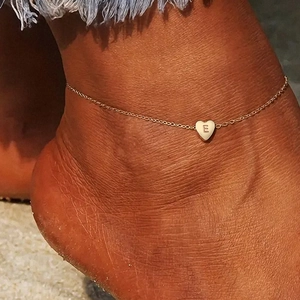 Detail of rose gold heart pendant with letter E engraving on a beach foot chain