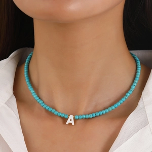 Turquoise bead necklace with shell initial A pendant and gold accents on a model