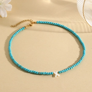 Detail of turquoise bead necklace featuring a white shell letter X pendant and gold clasp