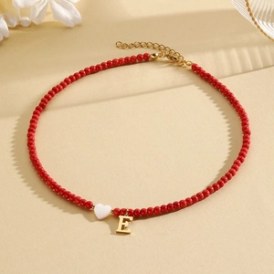 Detail of red beaded necklace featuring a white heart charm and gold-tone letter E pendant