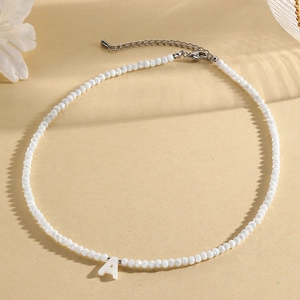 Faceted white beaded necklace with a silver metal letter A pendant on beige background