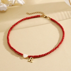 Detail of red beaded necklace with golden letter R pendant and white heart charm