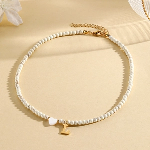 Macro shot of white marbled beaded necklace featuring a gold letter L and heart pendant