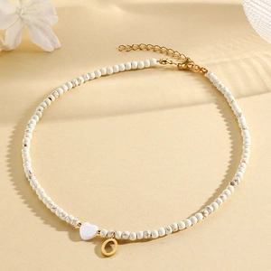 White beaded necklace with heart bead and gold letter O pendant on a beige background