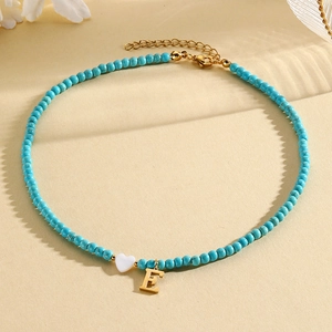 Macro shot of turquoise beaded necklace with white heart and gold initial E pendant