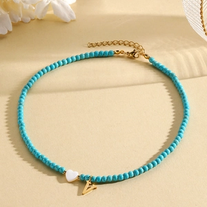 Detail of turquoise beaded necklace featuring white heart pendant and gold letter V charm
