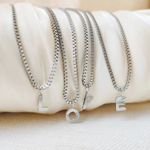 Detailed view of silver LOVE letter pendants with radial texture on elegant satin background