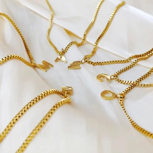 Macro detail of gold initial pendants with textured engraving on a box chain