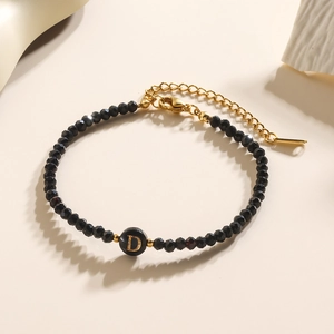 Detailopname van een zwarte facetgeslepen kralenarmband met een gouden letter D-bedel en slot