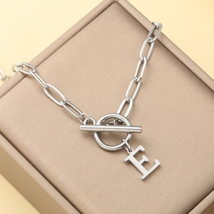 Collar de clip plateado con cierre OT y colgante de letra E sobre joyero elegante