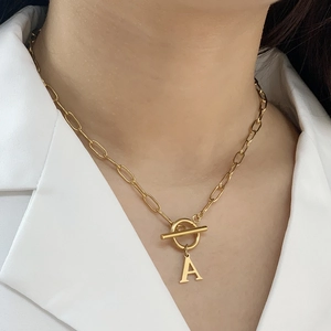 Collar de clip dorado con cierre OT y colgante de letra A sobre una camisa blanca
