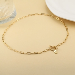 Collar de cadena dorada con cierre de barra y colgante de letra C sobre fondo beige