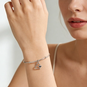 Detail van zilveren hartarmband met metalen kralen om de pols van een vrouw