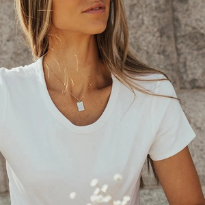 Close-up of minimalist square gold pendant necklace worn by a model against stone wall
