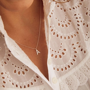 Vue détaillée d'un collier pendentif lettre A en argent poli porté par un modèle