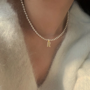 Vintage pearl necklace with a gold-tone cubic zirconia letter R pendant on a model
