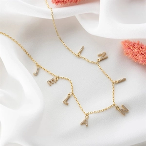 Detail of gold name necklace with micro-pave zircon letters on soft white silk