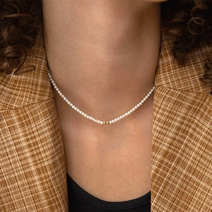 Close-up of minimalist pearl necklace with gold beads on female model in blazer