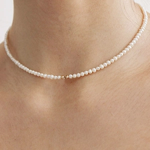 Close-up of a minimalist pearl choker necklace with gold beads on a woman's collarbone