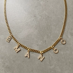 Nahaufnahme einer goldenen Panzerkette mit Zirkon-besetzten Buchstaben EMANCO auf Stein