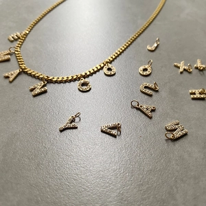 Details einer goldenen Panzerkette mit funkelnden Zirkonia-Buchstabenanhängern für Damen