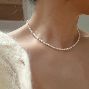 Elegante collana di perle ovali minimalista per donna indossata su maglione bianco