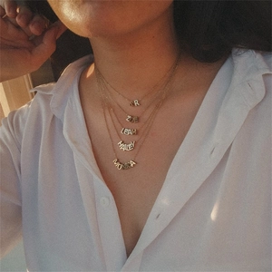 Detailopname van gelaagde gouden kettingen met gepersonaliseerde letterhangers bij een model
