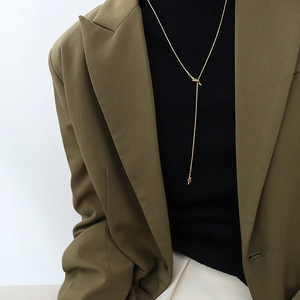 Detail of a long gold knotted tassel necklace styled on a black turtleneck and green blazer