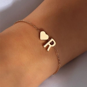 Detail of a gold plated cross chain bracelet featuring a heart charm and letter R pendant