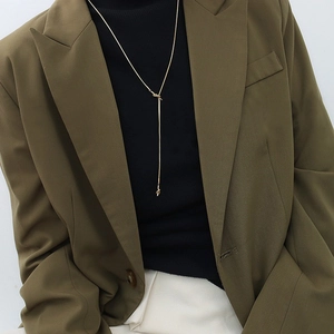 Detail of a gold-tone knot tassel necklace styled on a chic office outfit with a blazer