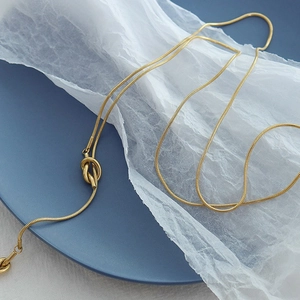 Close-up of golden snake chain necklace with decorative knot detail on textured fabric