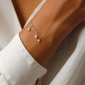 Nahaufnahme eines minimalistischen Gold-Titanstahl-Armbandes mit drei weißen Perlen am Handgelenk