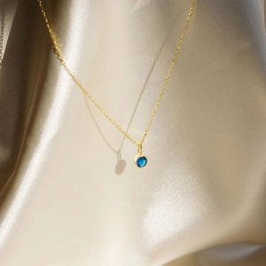 Detail eines runden blauen Zirkon-Anhängers an einer feinen Goldkette auf Seide