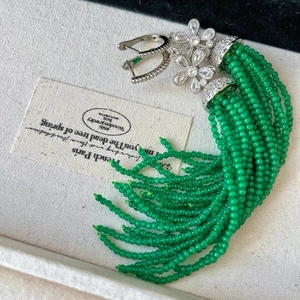 Detail view of silver flower earrings with long bright green beaded tassels and zircons