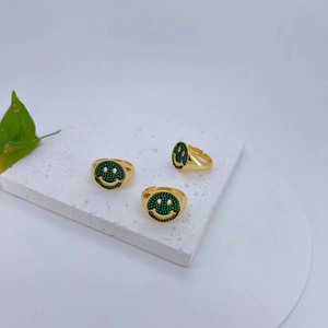 Detailweergave van drie gouden ringen met groene zirkoon smiley op een stenen plaat