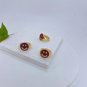 Detail van drie vergulde smiley-ringen met rozerode steeninleg op een marmeren voet