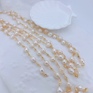 Detail of layered gold chain with Baroque pearls and round zircon on a white shell tray