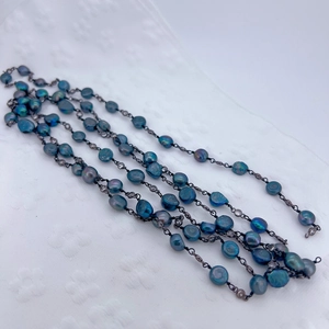 Detail of peacock blue freshwater pearls and zircon beads on a long woven necklace