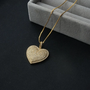 Macro detail of a heart-shaped gold pendant with cubic zirconia pavé setting on black silk