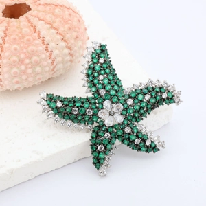 Starfish brooch with green and white cubic zirconia on a white stone background