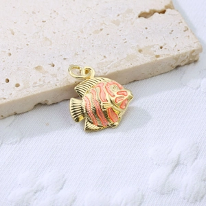 Detail of a gold copper fish pendant with orange enamel stripes on a stone surface