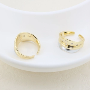 Close-up of dual-tone gold-plated open rings with inlaid white zircons in a ceramic dish