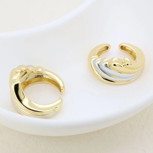 Macro view of gold and silver plated wave-textured open ring set on ceramic tray