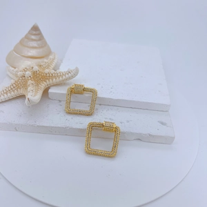 Modern gold square earrings with pavé zircons on a white textured stone display